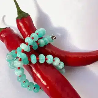 close-up shot of handmade necklace made using button shaped beads of blue agate stones with tiny red glass beads. trending chunky beaded necklace for summer