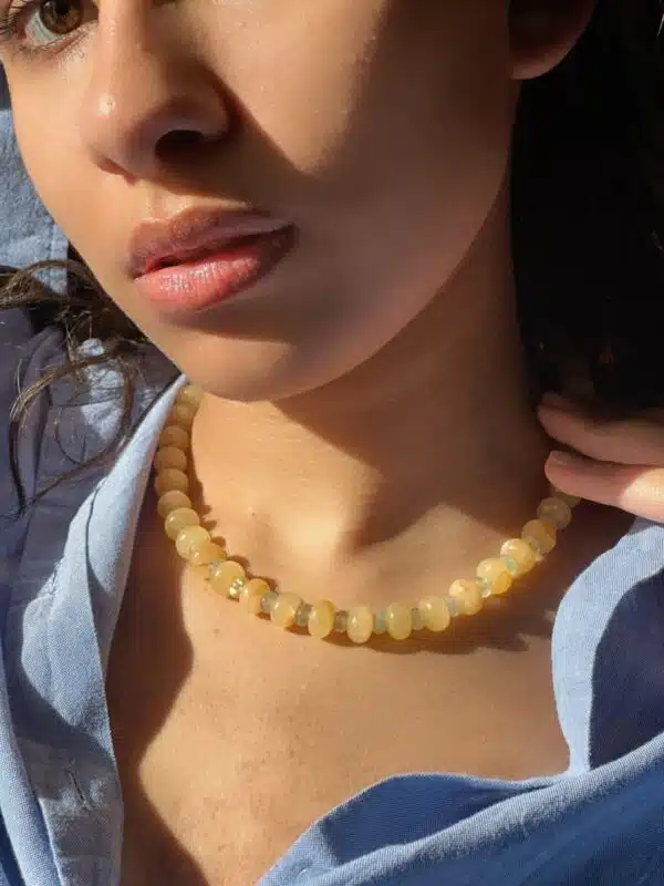 try on shot of the hand-beaded Citrine Skies Necklace No.02 in butter yellow agate stones and tormaline blue stones A soft summer day, captured in stone.Inspired by the golden warmth of citrine sunsets and the tranquility of clear skies. Blends butter yellow and sky blue tones in a dreamy, refreshing palette. Handcrafted with natural jade and tormaline gemstones and finished with 925 sterling silver clasp. Featuring: Material: Natural jade stones - Length: 42 cm - 925 sterling silver clasp