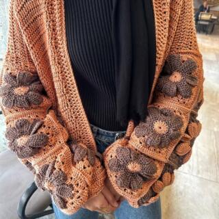 Handmade crochet cardigan featuring large 3D floral granny-square patterns in warm orange and brown tones.