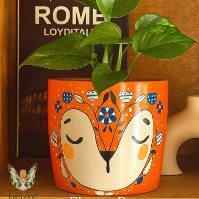 Sleepy FOX Planter Pot 1 أصيص زرع فخار برتقالي مرسوم عليه وجه ثعلب نائم بنقوش زهور. | Orange clay planter featuring a sleeping fox face with floral patterns.
