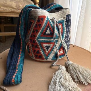 Handmade crochet mochila bag with geometric patterns, adjustable crossbody strap, and tassel drawstring, crafted from cotton yarn in blue, terracotta, and neutral tones