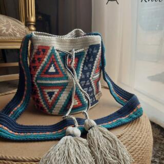 Handmade crochet mochila bag with geometric patterns, adjustable cross body strap, and tassel drawstring, crafted from acrylic yarn in blue, terracotta, and neutral tones.