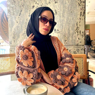 Handmade crochet cardigan featuring large 3D floral granny-square patterns in warm orange and brown tones.