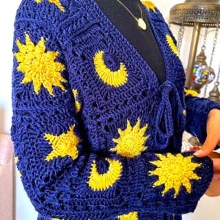 Navy blue crocheted cardigan featuring yellow sun, moon, and star motifs, with textured knit details and front pockets.