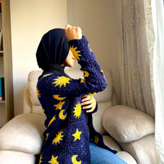 Navy blue crocheted cardigan featuring yellow sun, moon, and star motifs, with textured knit details and front pockets.