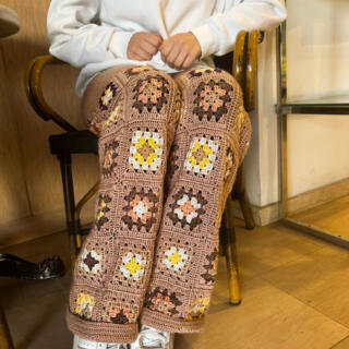 Beige nude wide-leg crochet pants with multicolor floral square pattern and flared hem.