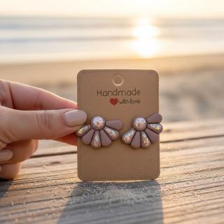 Handmade polymer clay daisy flower earrings with a fan-shaped design and glitter details in soft nude color, displayed on a card by the beach at sunset