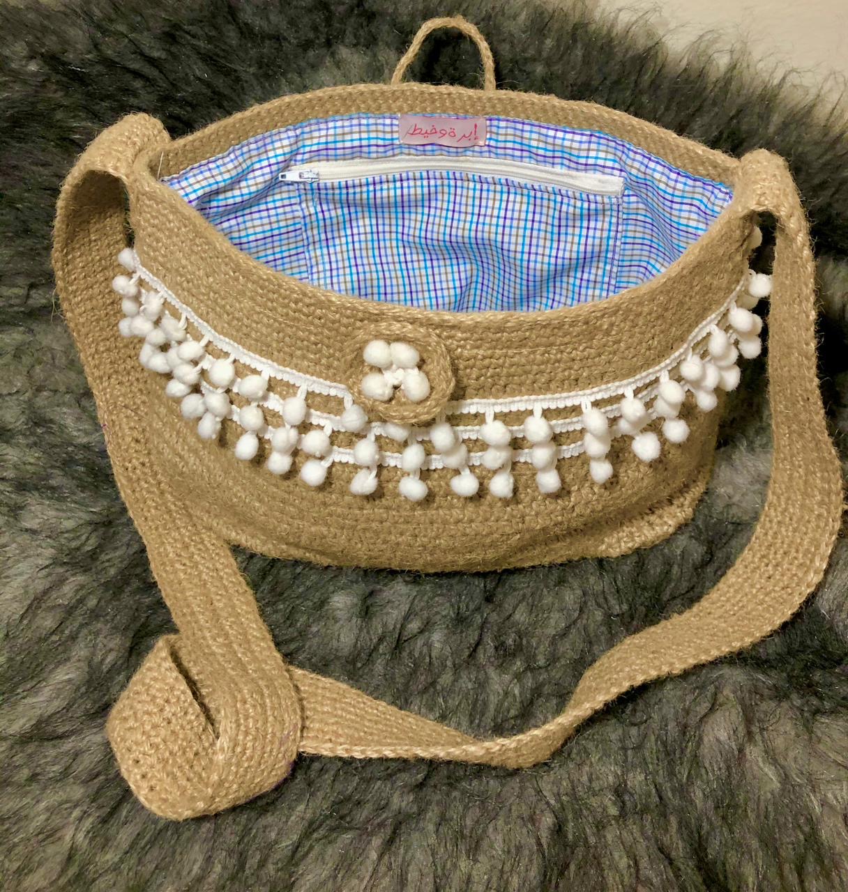 Pearl Pom Jute Tote 2 Handcrafted jute sling bag with white pom-pom trim, long woven strap, and soft checked fabric lining.