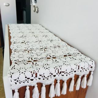 Handmade white crochet table runner with floral patterns and tassel edges displayed on a wooden table.