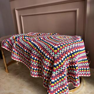 Colorful handmade crochet blanket with a classic granny square pattern draped over a chair in a cozy indoor setting.