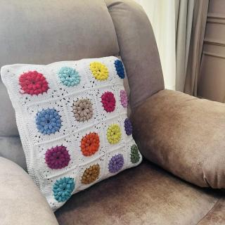 Colorful handmade crochet flower pillow with textured floral squares on a white base.