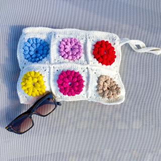 Handmade crochet pouch featuring textured floral granny square patterns stitched together on a soft white base with a drawstring closure.