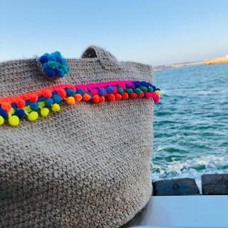 Handmade jute crochet tote bag with colorful pom-pom trim and sturdy shoulder straps.