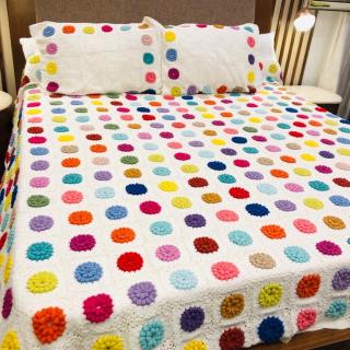 White textured bedding covered with vibrant multicolored soft circles, paired with matching pillows in a warm and stylish bedroom setting.