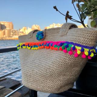 Handmade jute crochet tote bag with colorful pom-pom trim and sturdy shoulder straps.