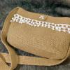 Handcrafted jute sling bag with white pom-pom trim, long woven strap, and soft checked fabric lining.