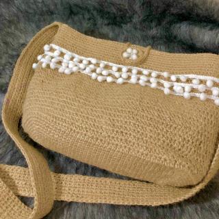 Handcrafted jute sling bag with white pom-pom trim, long woven strap, and soft checked fabric lining.